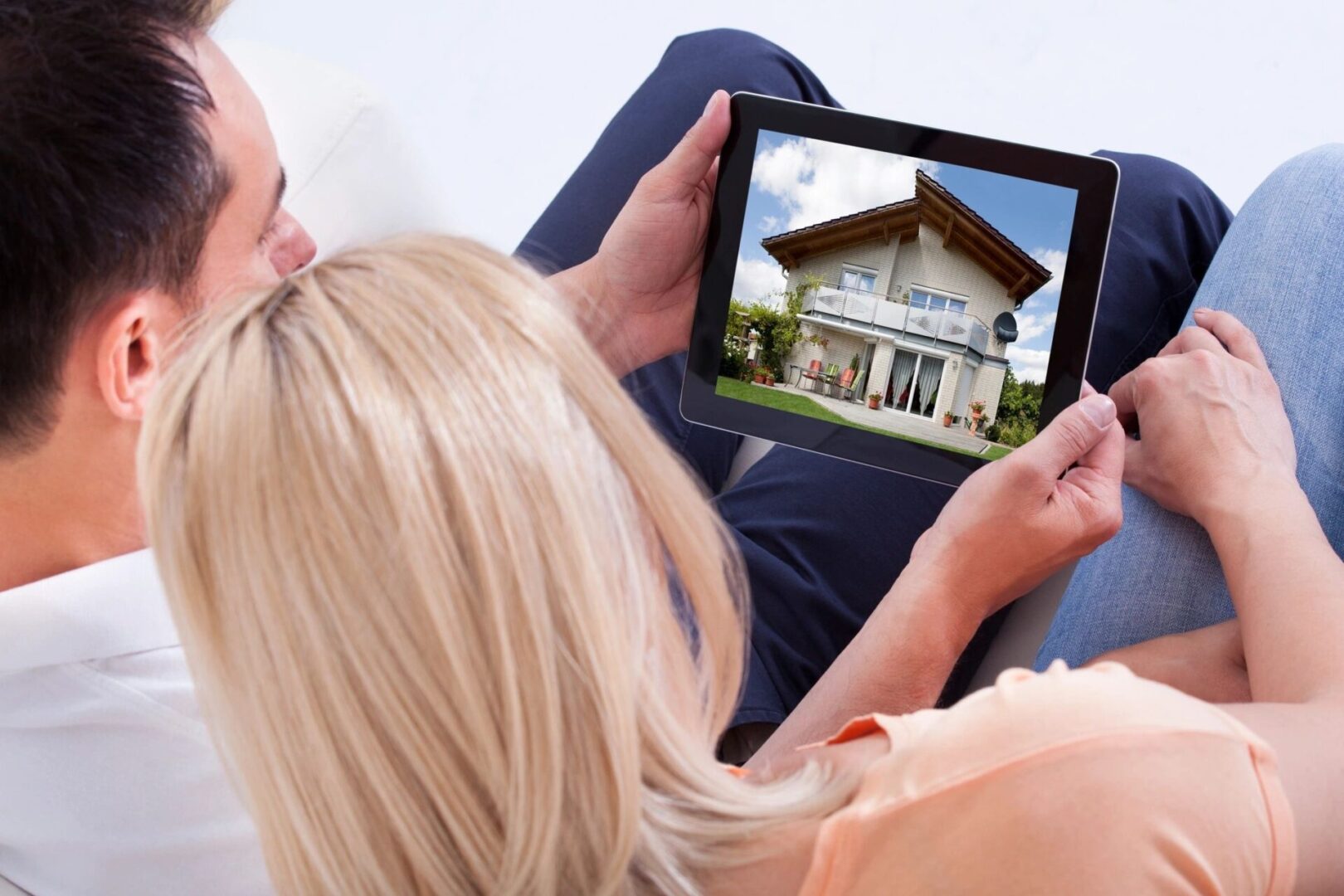 A man and woman looking at a photo of a home through a tablet